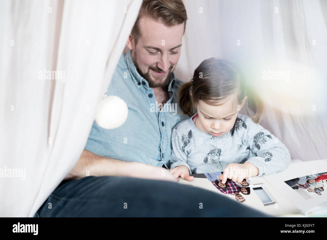 Father and daughter looking at photo album in toy teepee Stock Photo