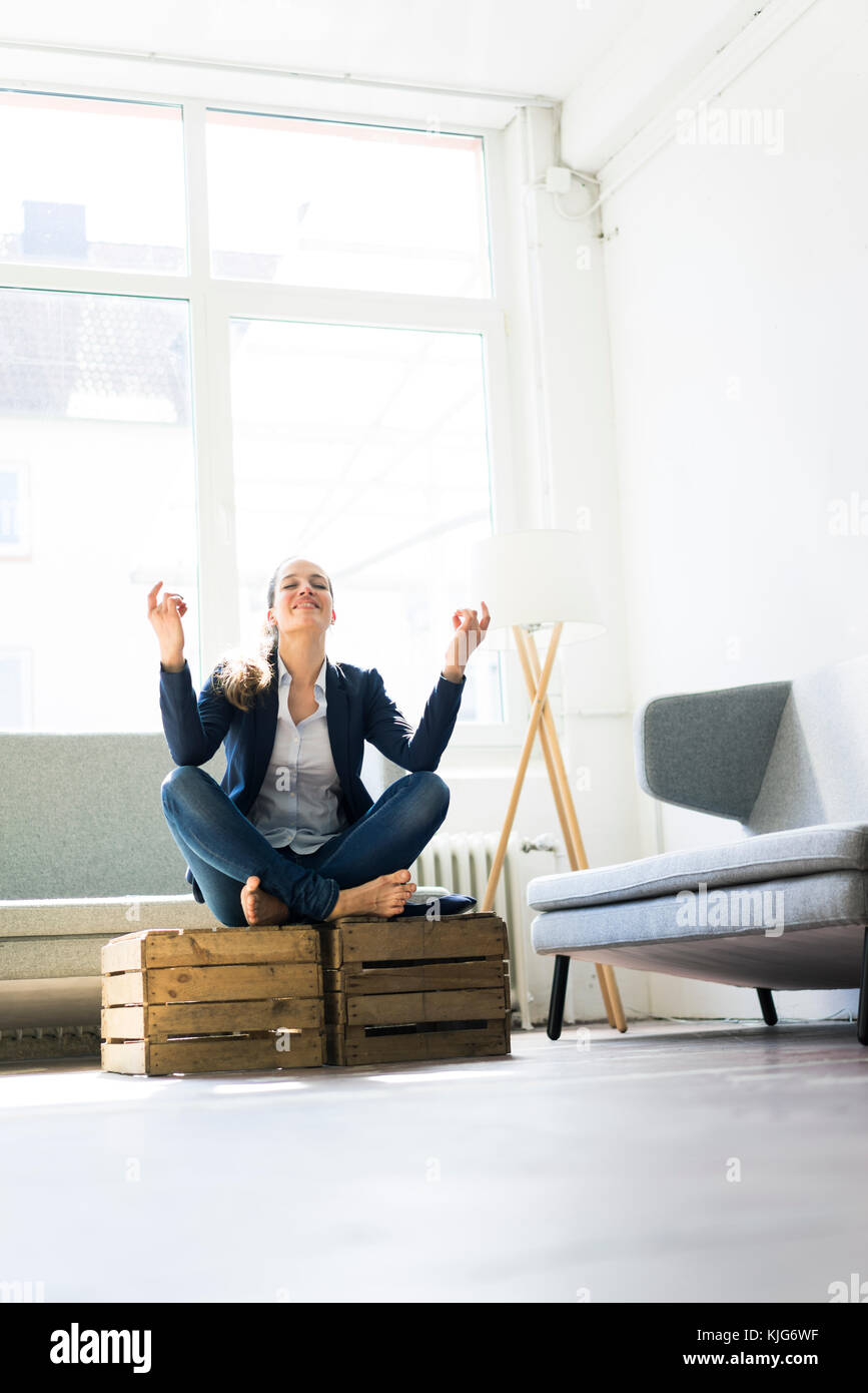 Businesswoman sitting on crate practising yoga Stock Photo