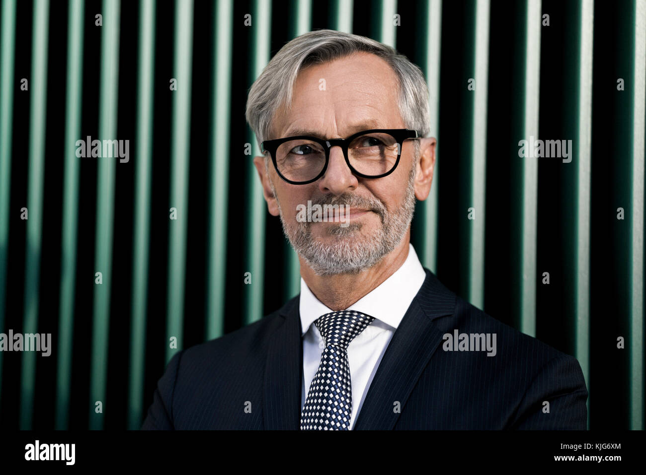 Portrait Of Grey haired Businessman In Front Of Green Wall Stock Photo