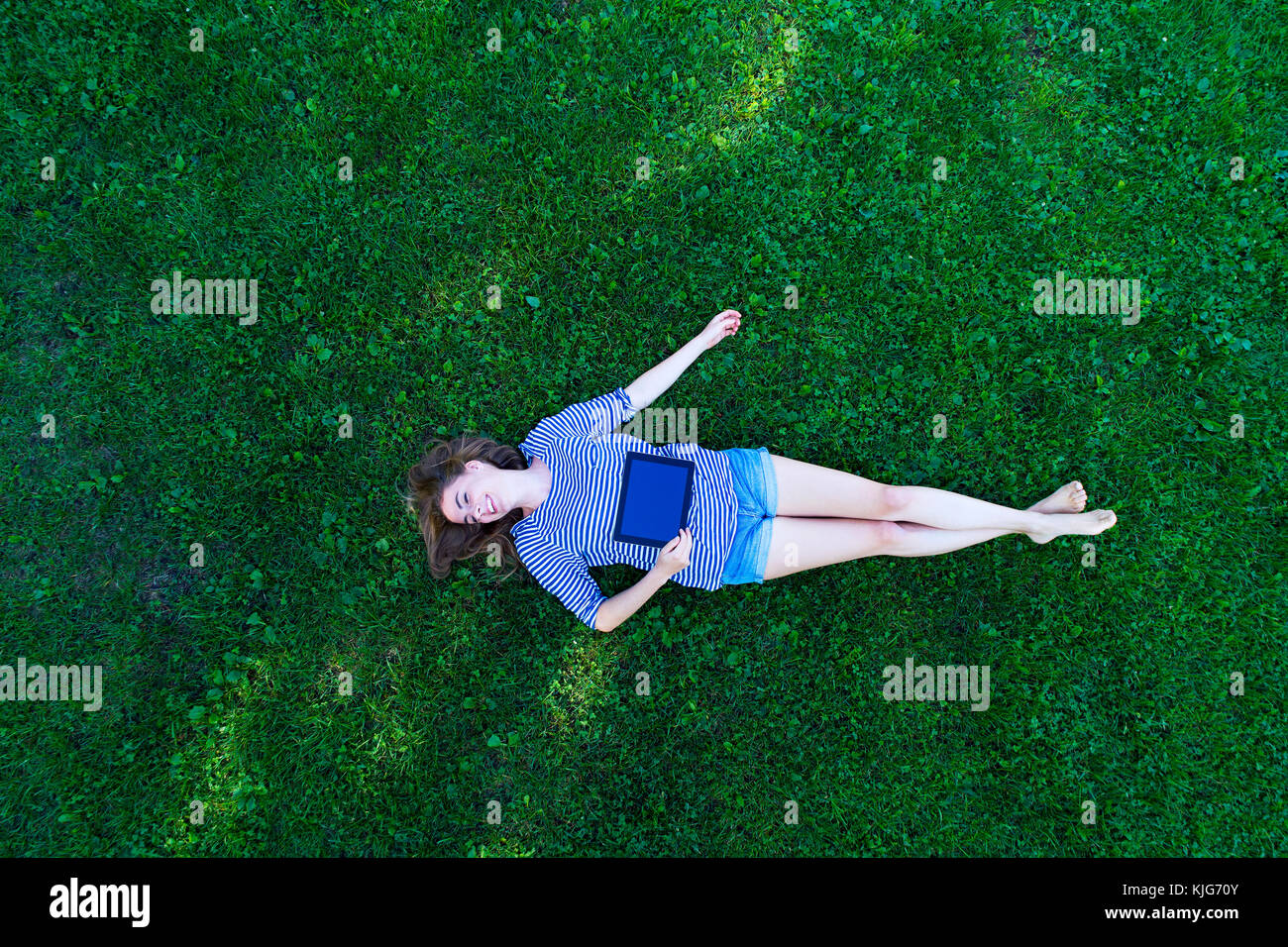 Young woman lying on grass, holding digital tablet Stock Photo - Alamy