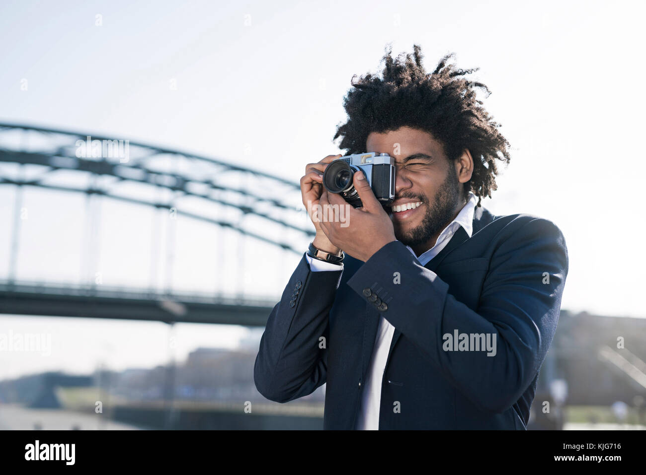Smiling man in suit at the riverside taking a picture with a vintage camera Stock Photo