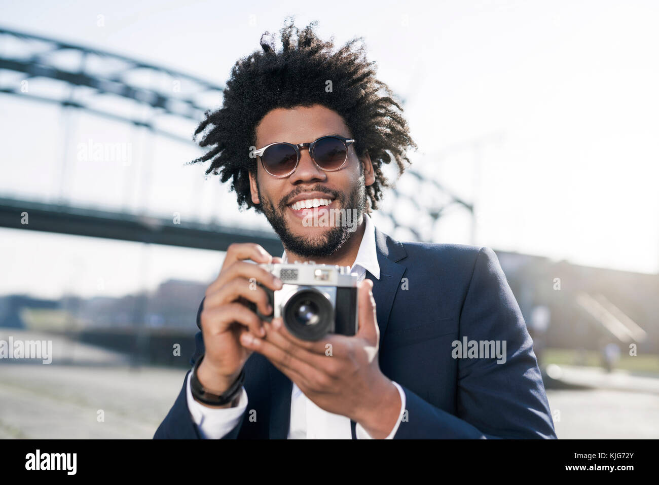 Smiling man in suit at the riverside holding a vintage camera Stock Photo