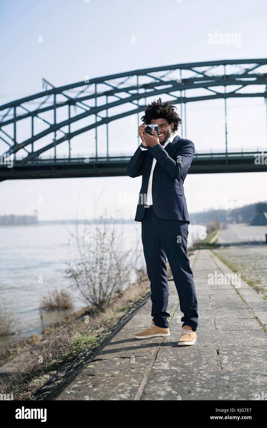 Smiling man in suit at the riverside taking a picture with a vintage camera Stock Photo