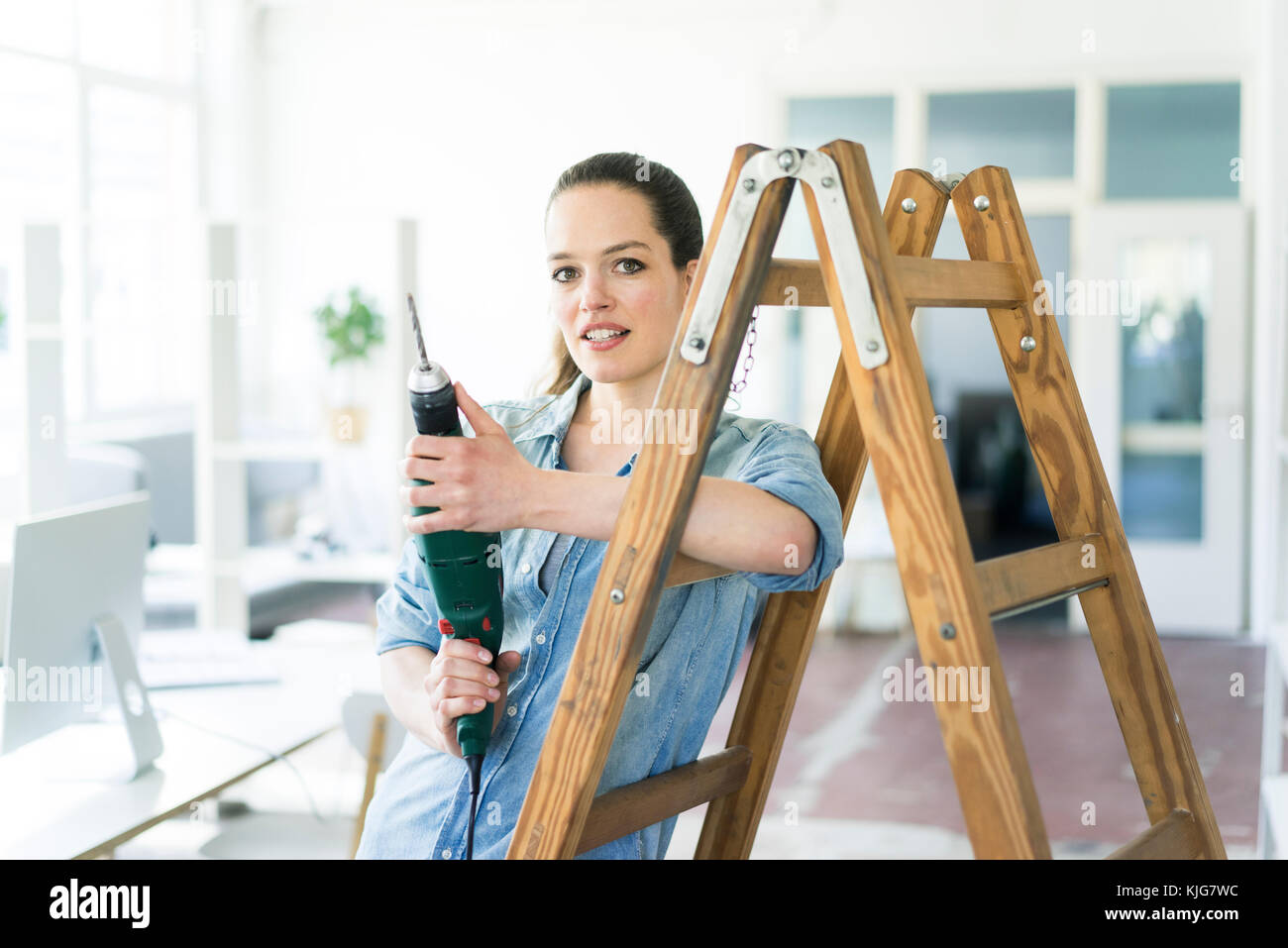 Portrait of woman at ladder holding electric drill Stock Photo