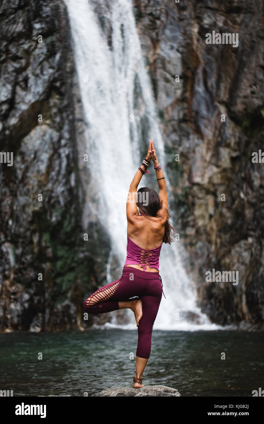 Woman doing tree yoga pose on rock near waterfall hi-res stock ...