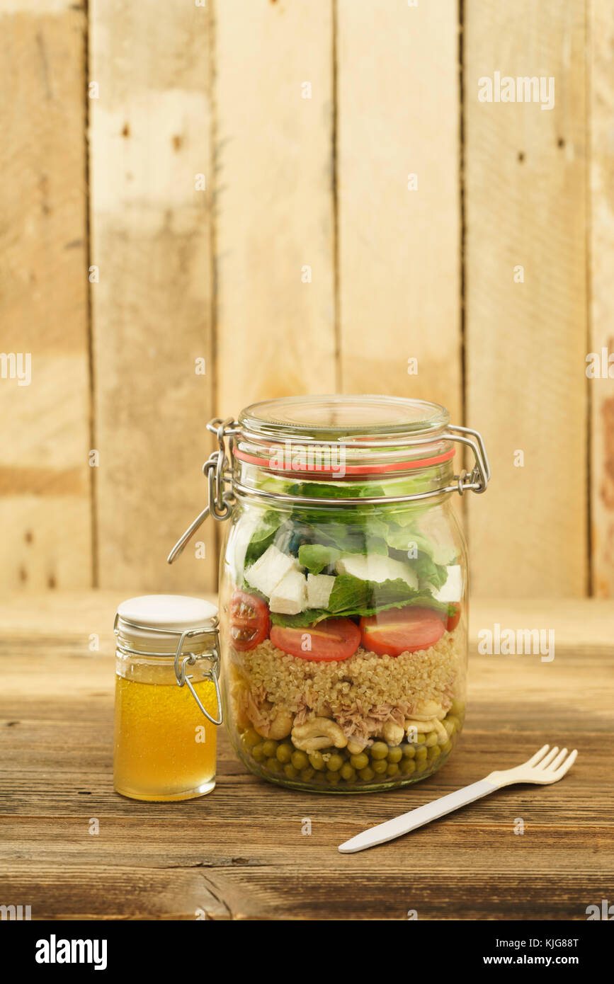 Salat zum Mitnehmen im Glas mit Erbsen, Cashew-Nüssen, Thunfisch, Couscous, Cocktailtomaten, Minze, Schafskäse, Blattsalat und Vinaigrette Stock Photo