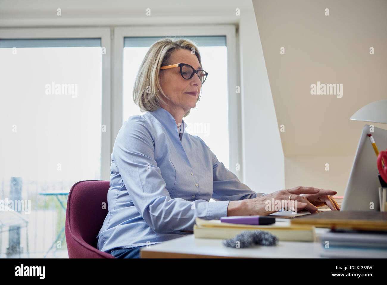 Mature woman at home using laptop at desk Stock Photo