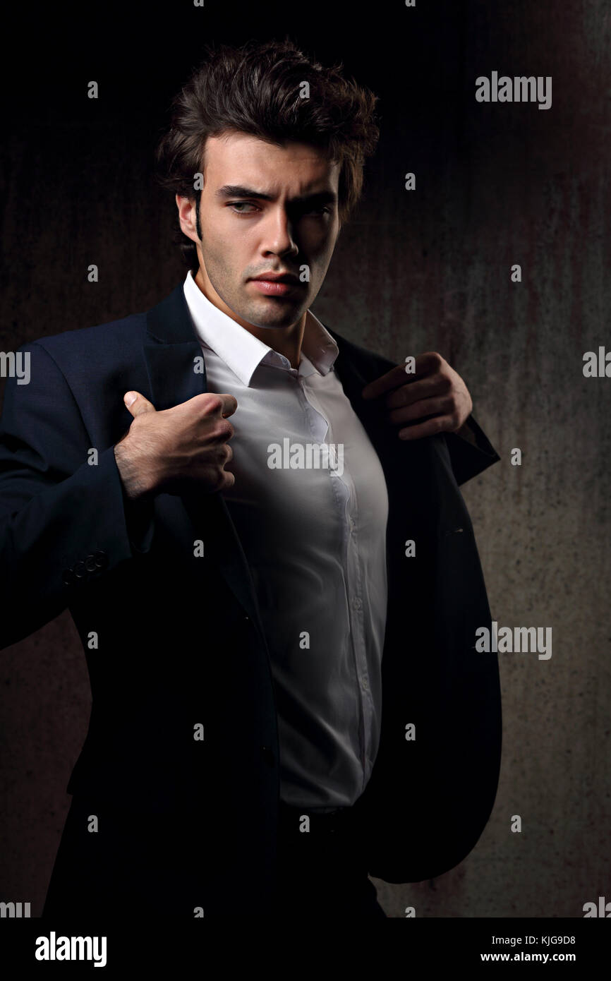Charismatic sexy male model posing and holding the fashion suit and white  style shirt looking energetic on dark shadow background. Closeup portrait  Stock Photo