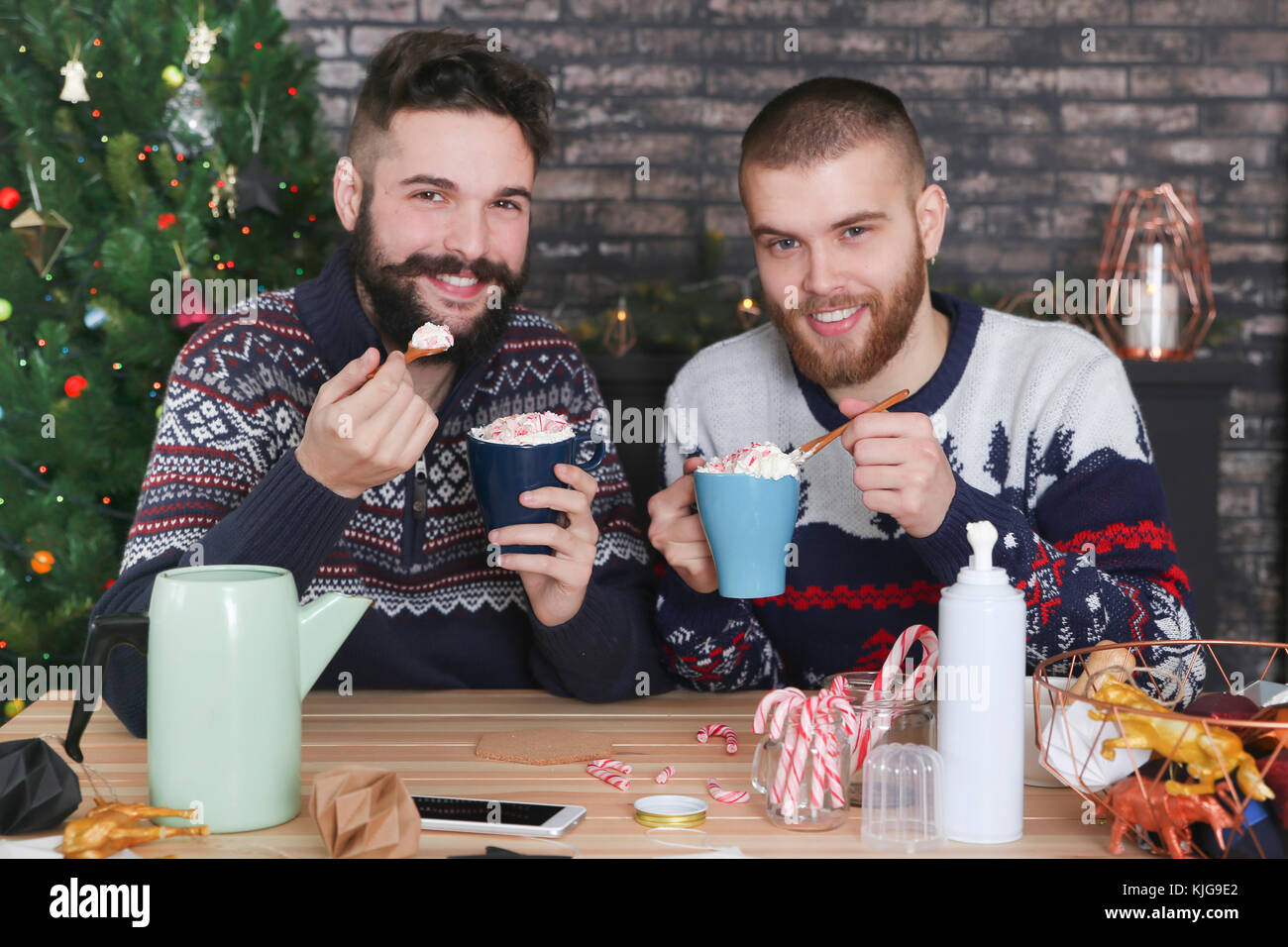 Happy gay couple drinking hot chocolate with cream and chopped candy canes at Christmas time Stock Photo