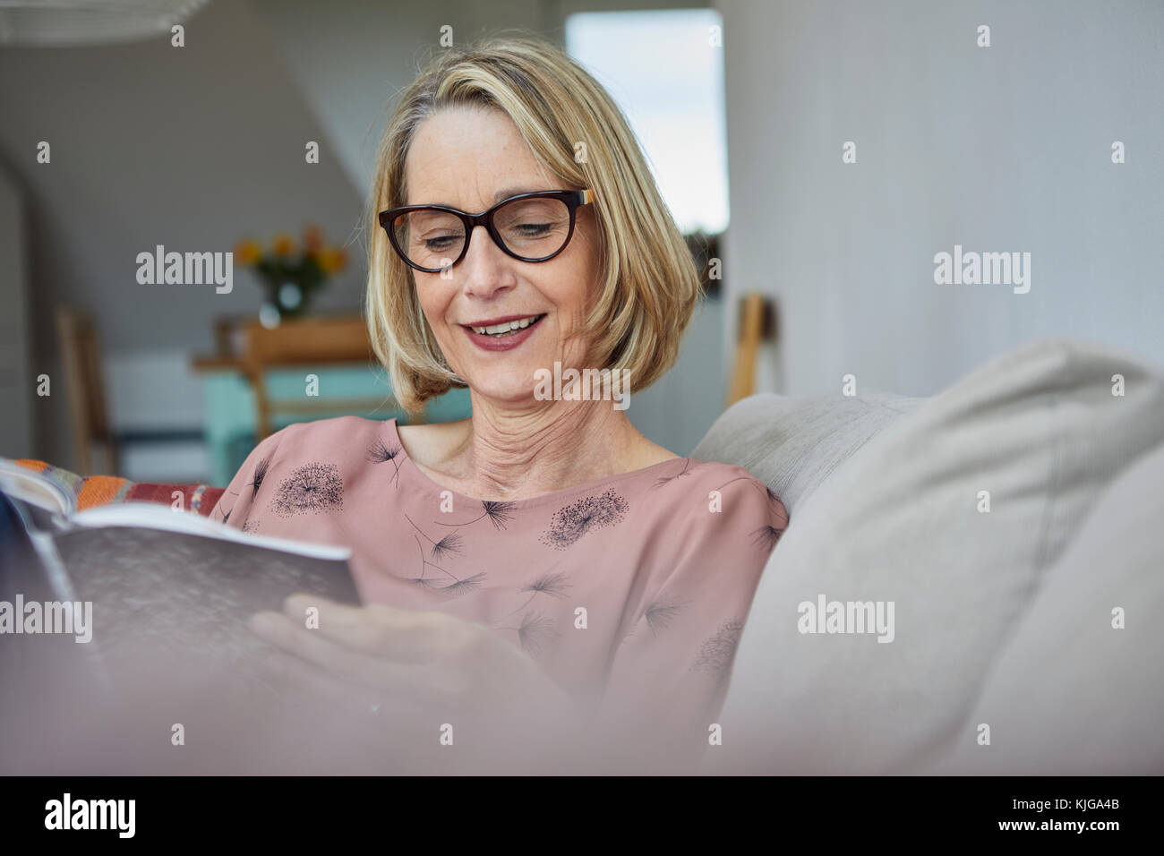 Smiling mature woman at home on the sofa reading a book Stock Photo