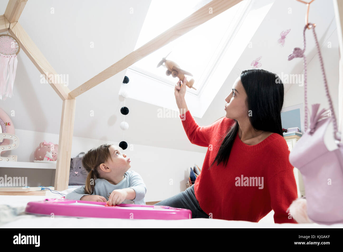 Mother and toddler daughter playing with toy plane in nursery Stock Photo