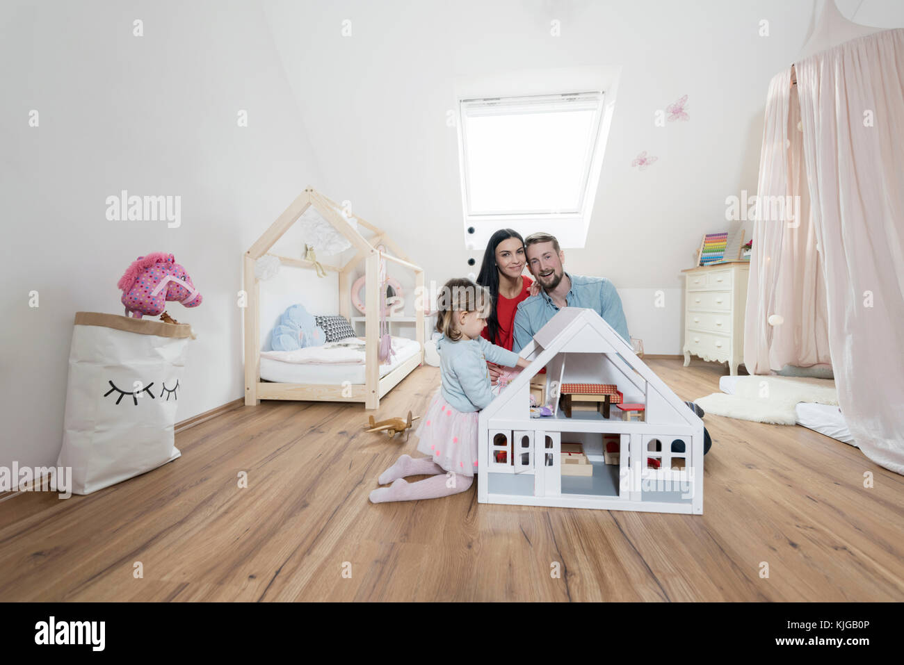 Happy parents in nursery while toddler daughter is playing with a doll house Stock Photo