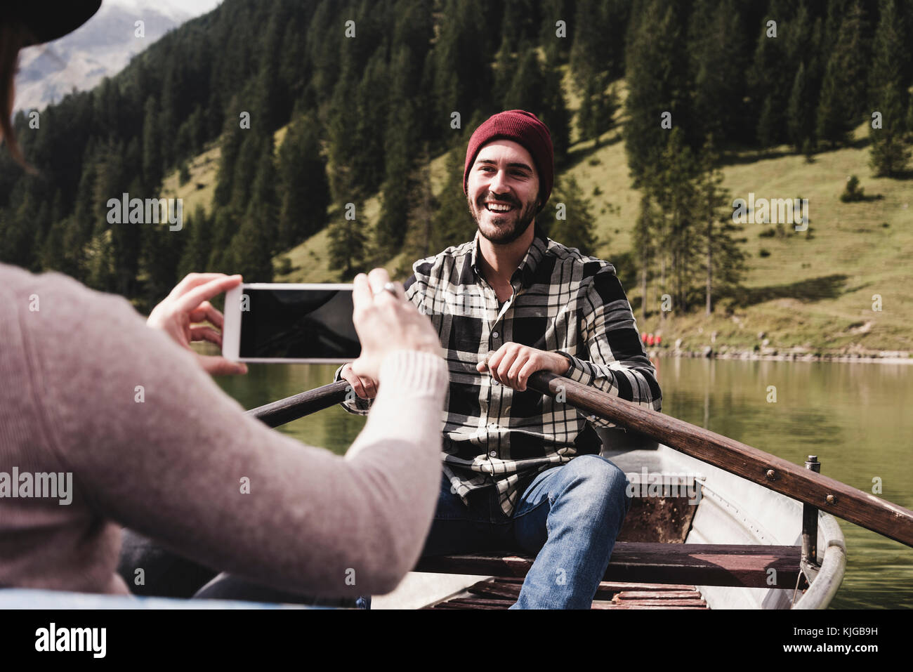 Austria, Tyrol, Alps, woman taking cell phone picture of smiling man in rowing boat on mountain lake Stock Photo