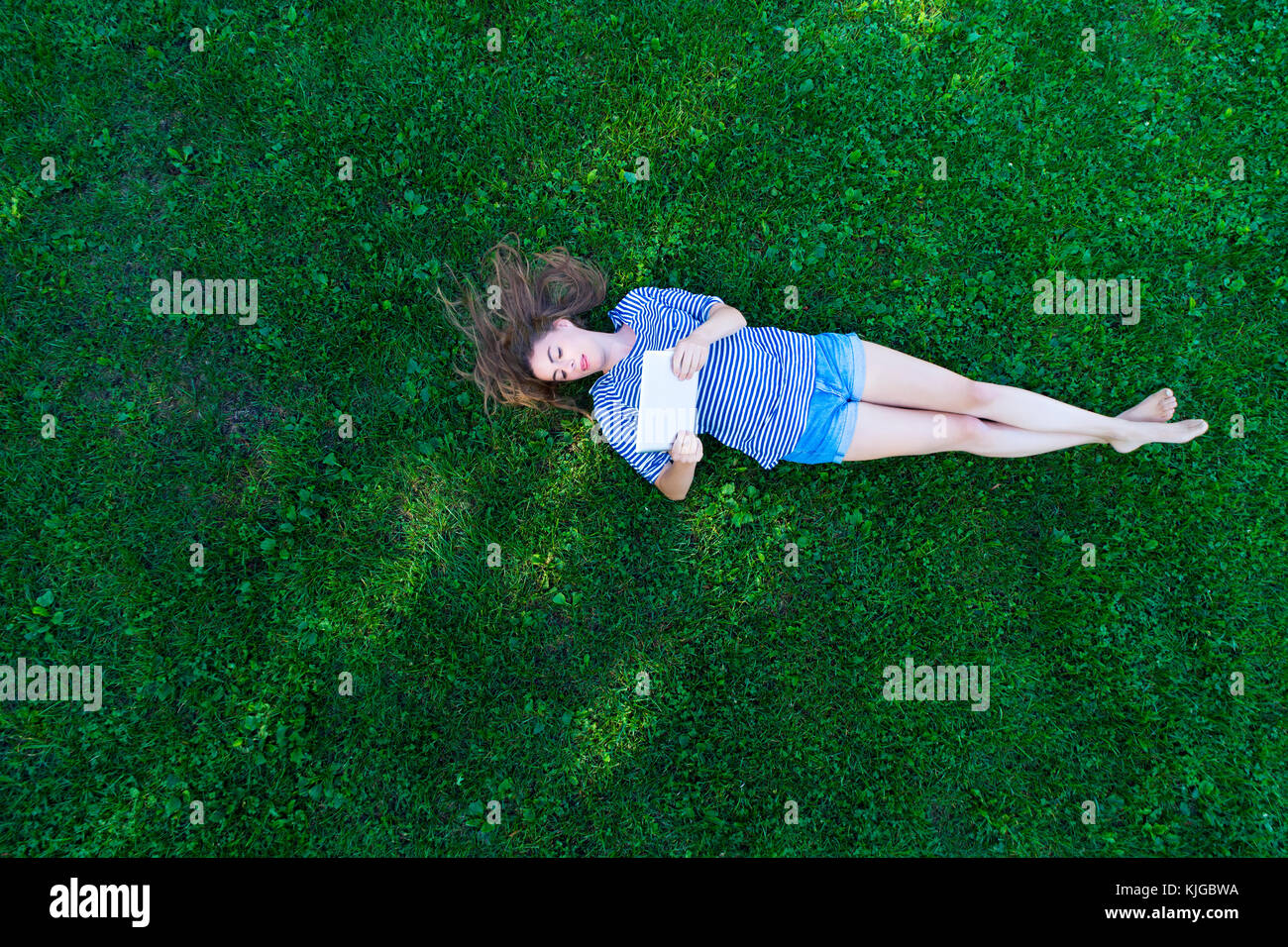 Young woman lying on grass, holding digital tablet Stock Photo - Alamy