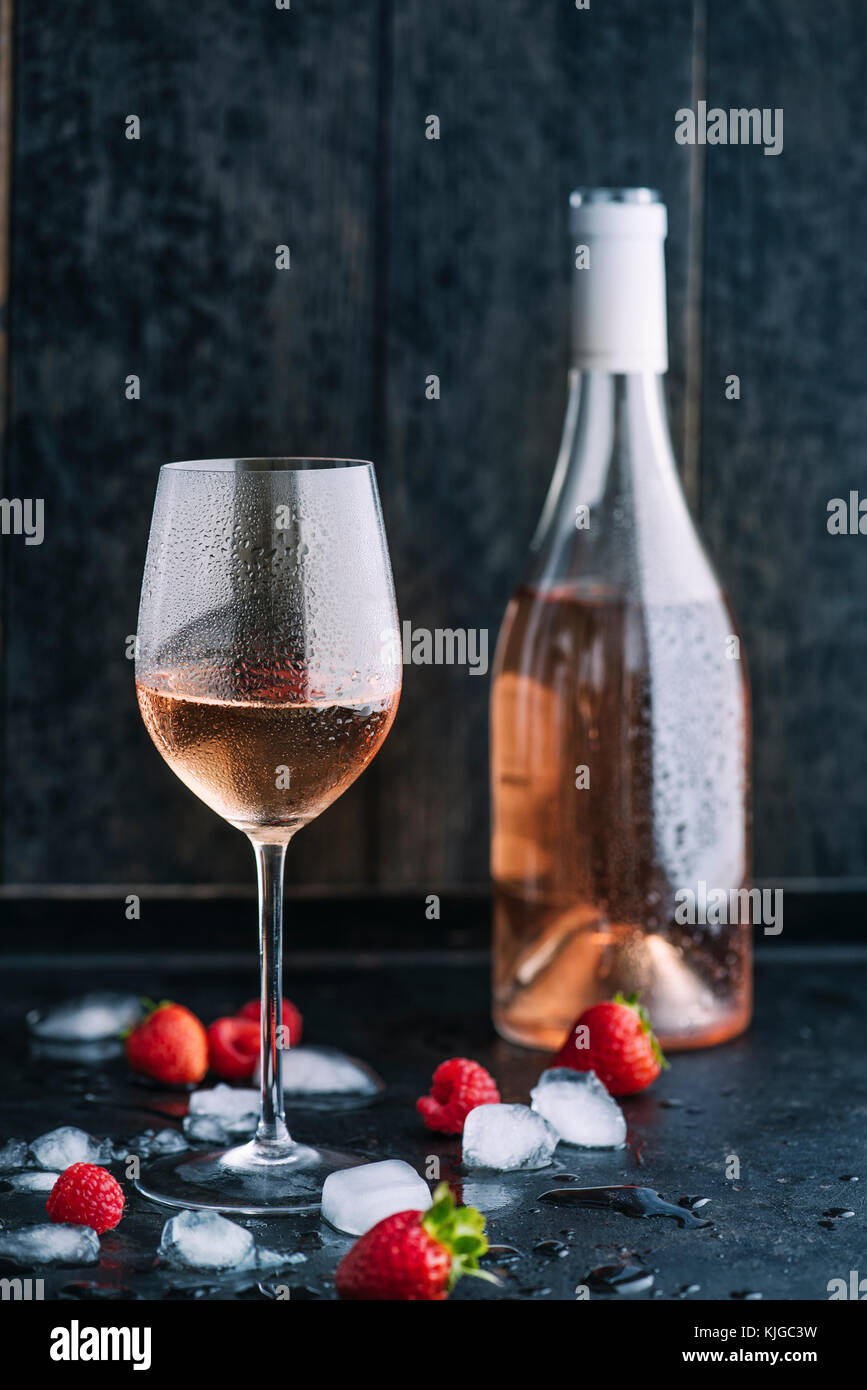 Rosé wine with ice cubes and fruits as aroma symbols on dark background