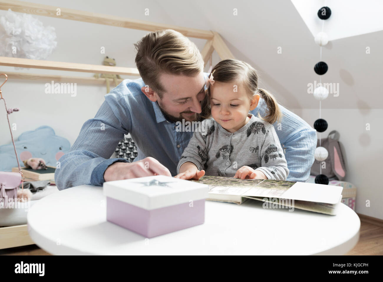 Father and daughter looking at photo album in her nursery Stock Photo
