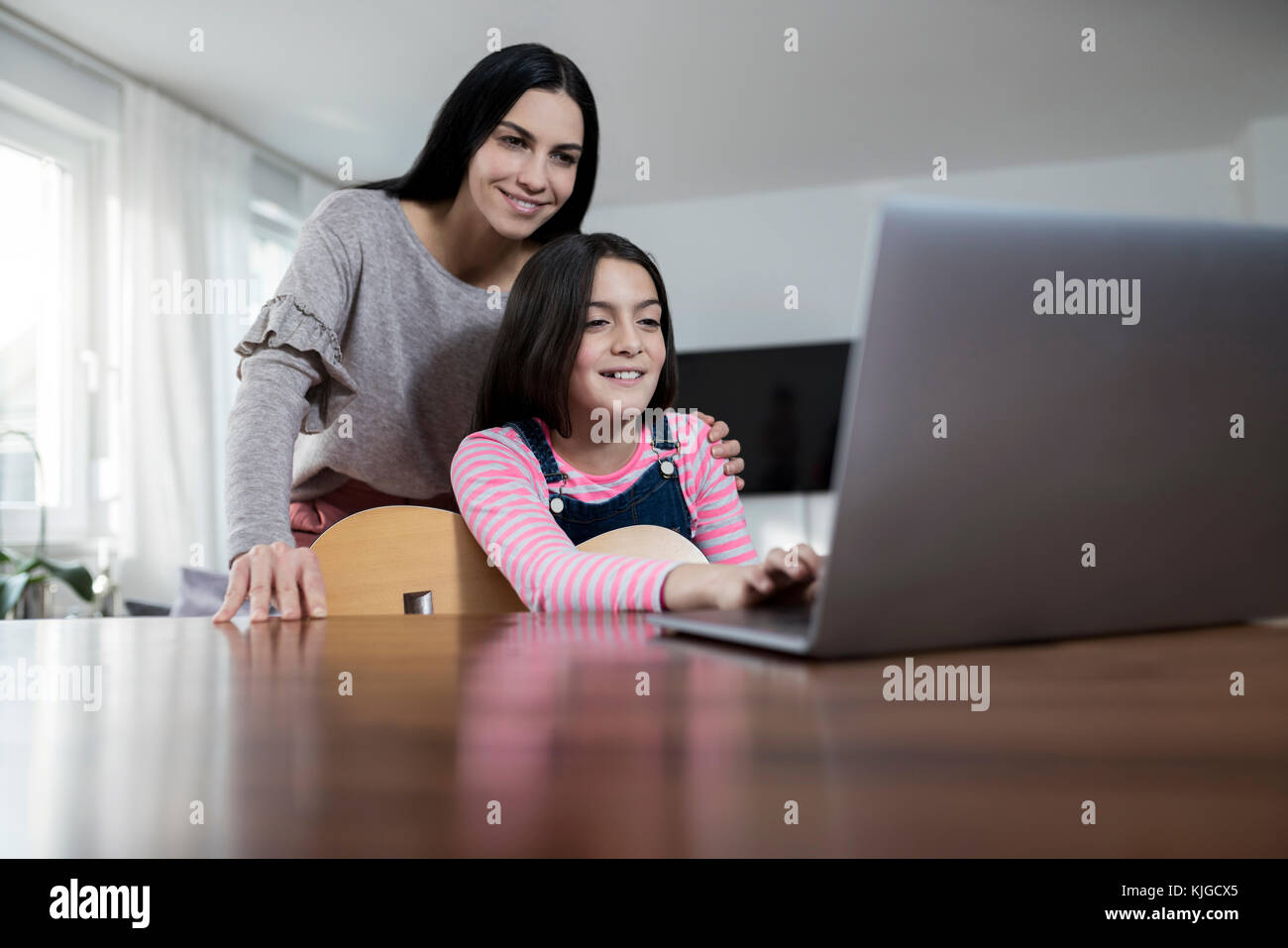Mother and daughter smiling in front of laptop with daughter holding a guitar Stock Photo