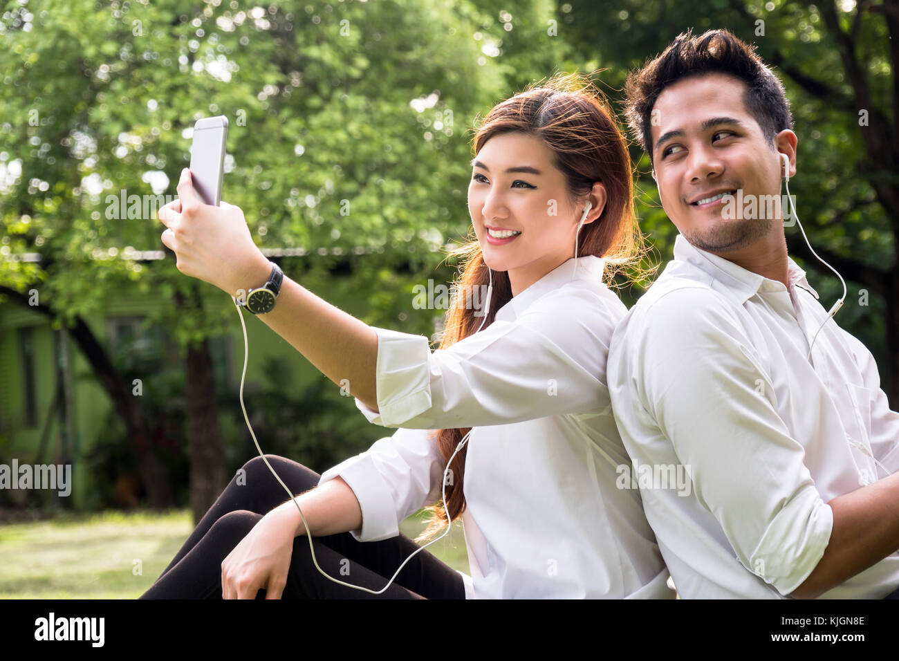 Happy asian couple taking a selfie with smart phone camera in the park ...