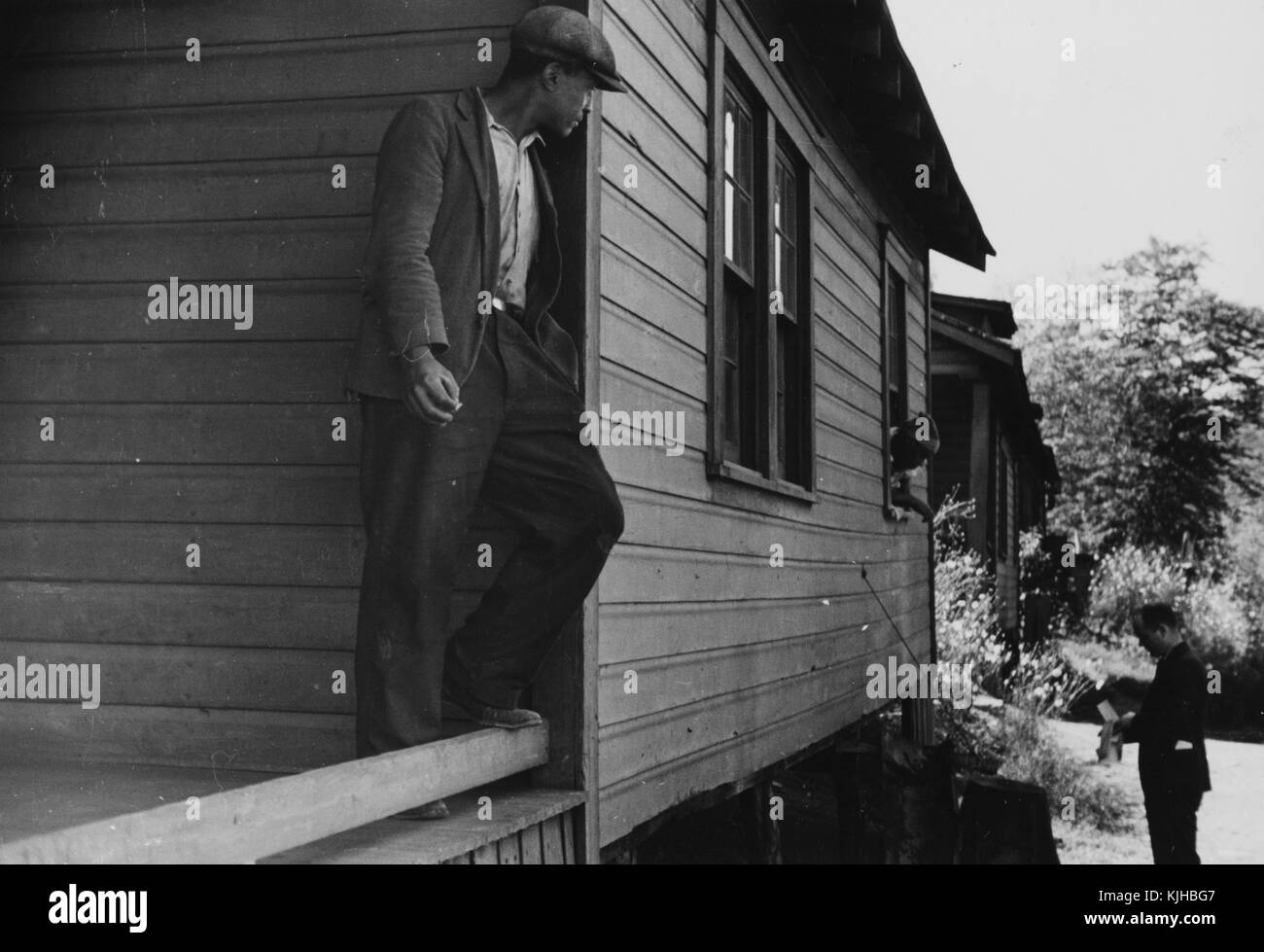 A photograph of an employee of the Farm Security Administration delivering a relief check to a farmer, the FSA relief checks were intended to improve the lives and farms of farmers around the country, a woman speaks to the man through an open window of her wooden home, a man stands on the porch smoking a cigarette while watching their interaction, Scott's Run, West Virginia, 1935. From the New York Public Library. Stock Photo