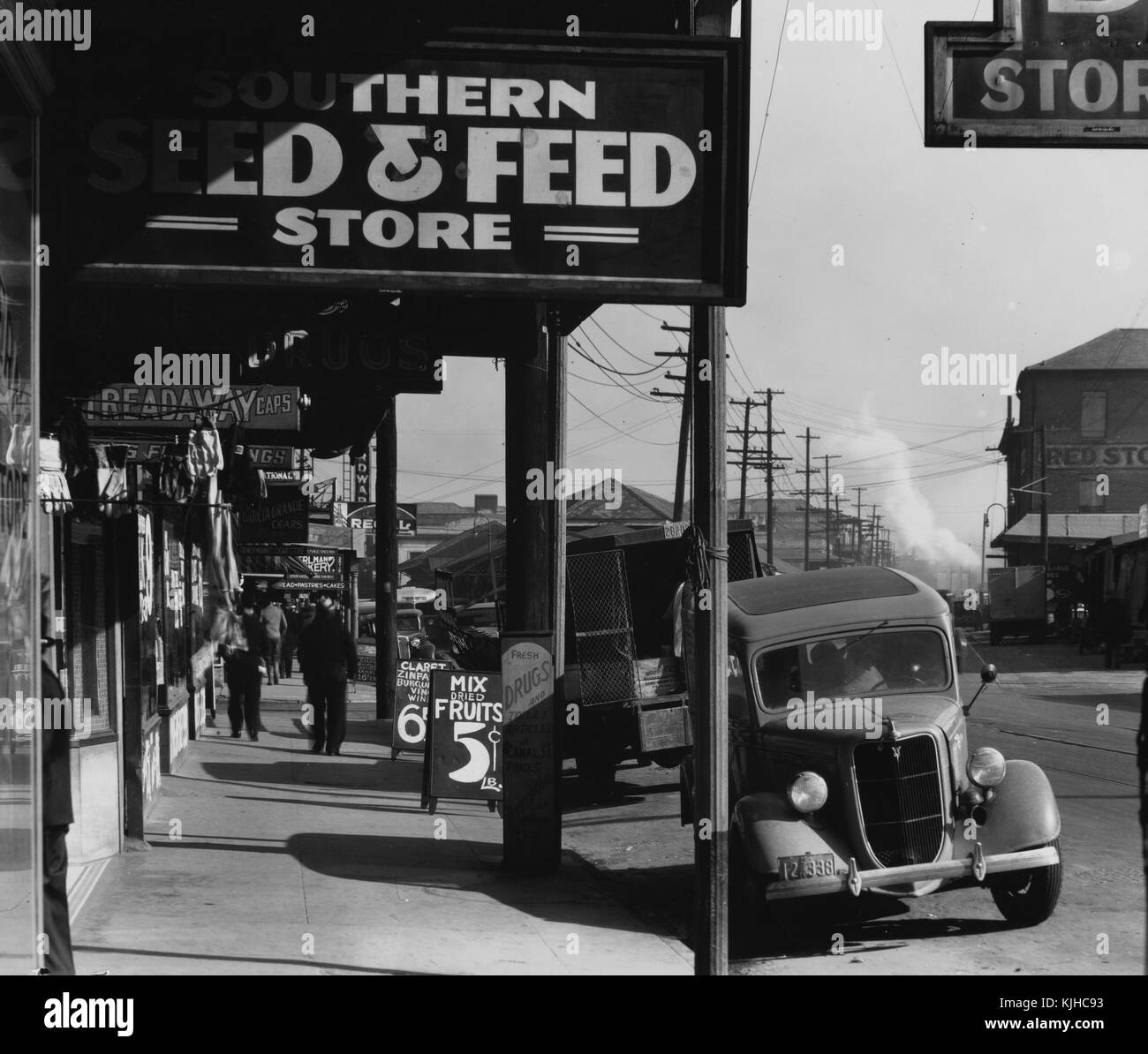 Black and white photograph of a sidewalk lined with stores, cars parked on the street, by Walker Evans, American photographer best known for his work for the Farm Security Administration documenting the effects of the Great Depression, New Orleans, Louisiana, 1935. From the New York Public Library. Stock Photo