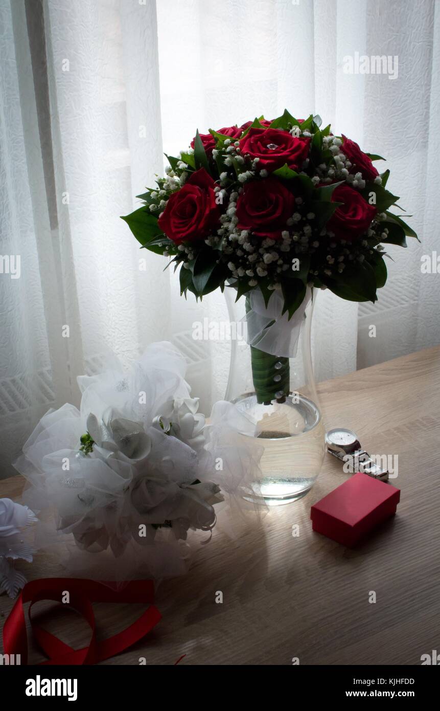 Red roses bride`s bouquet in the vase on wooden table with red box and ...