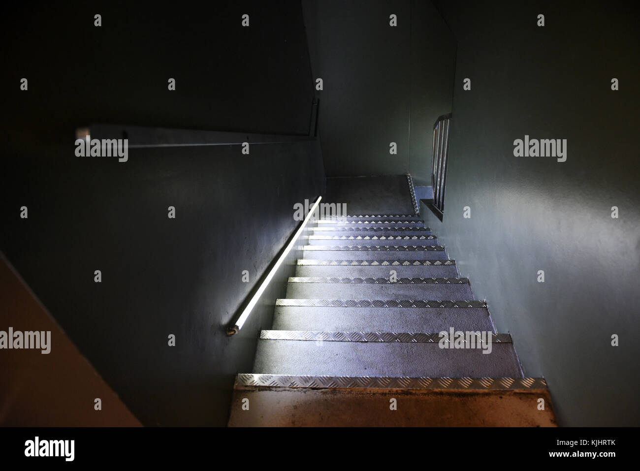 Steep flight of steps in a dark shadowy interior with an illuminated hand rail and metal edged treads Stock Photo