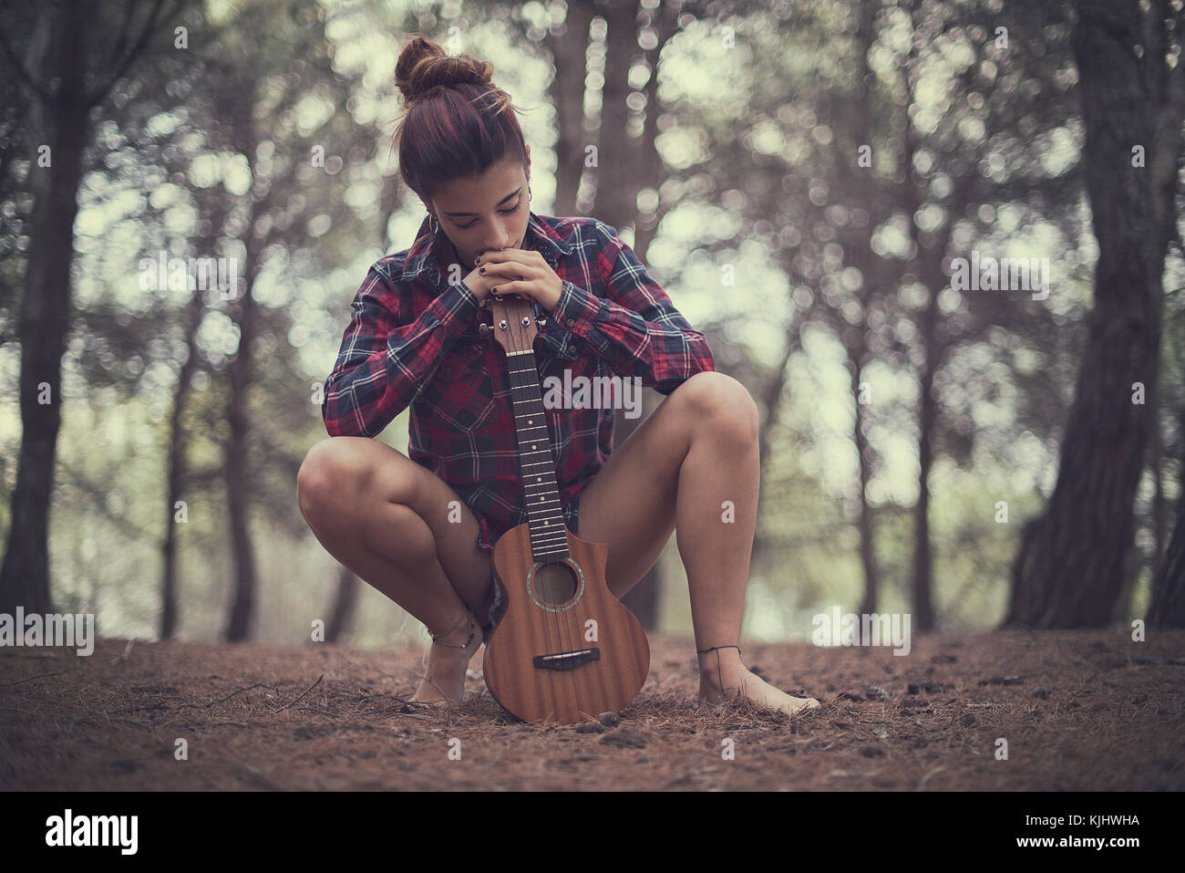 Teenage girl crouching in the forest with her ukulele Stock Photo