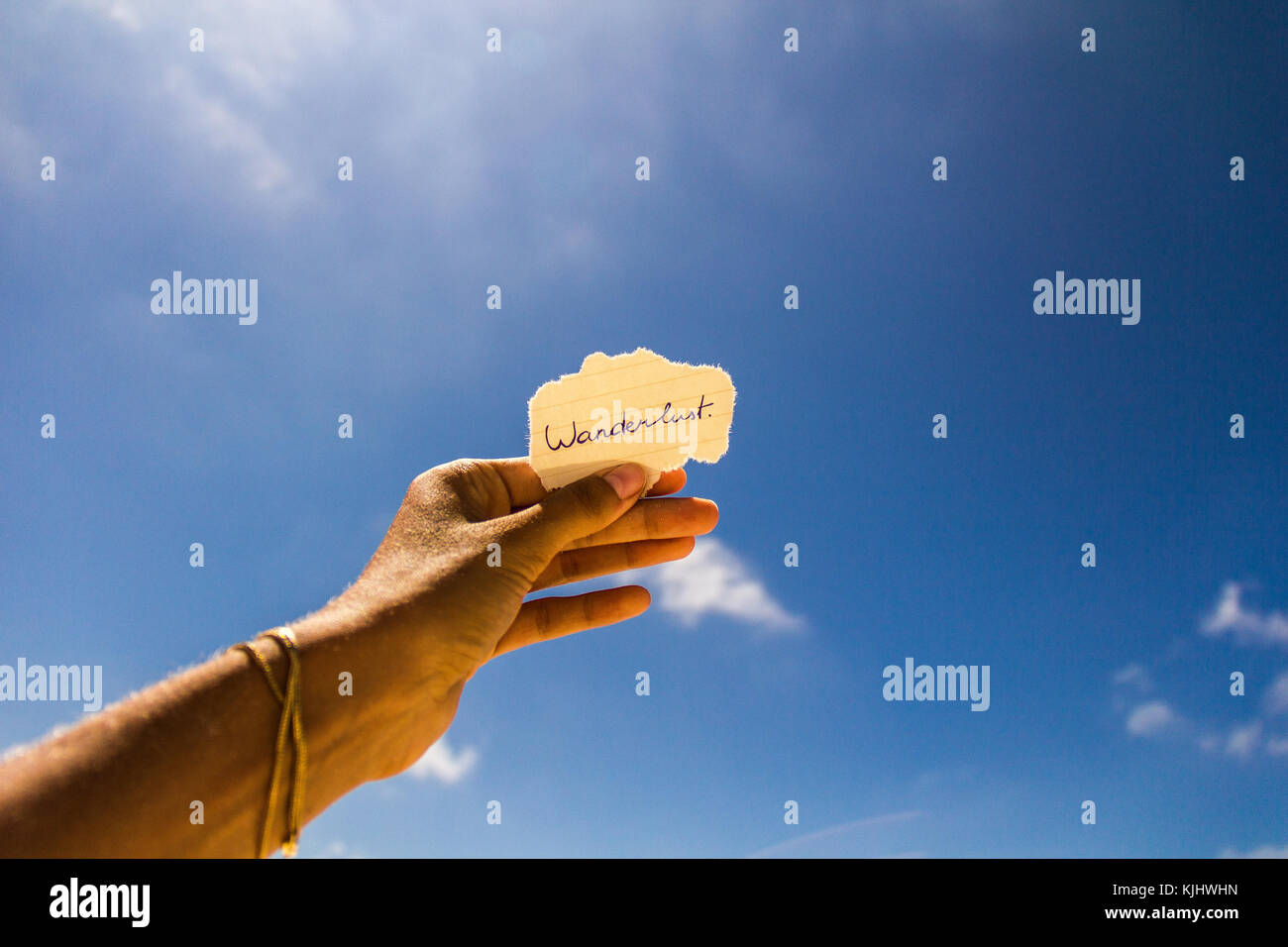 Woman's hand holding a piece of paper with the word wanderlust Stock Photo