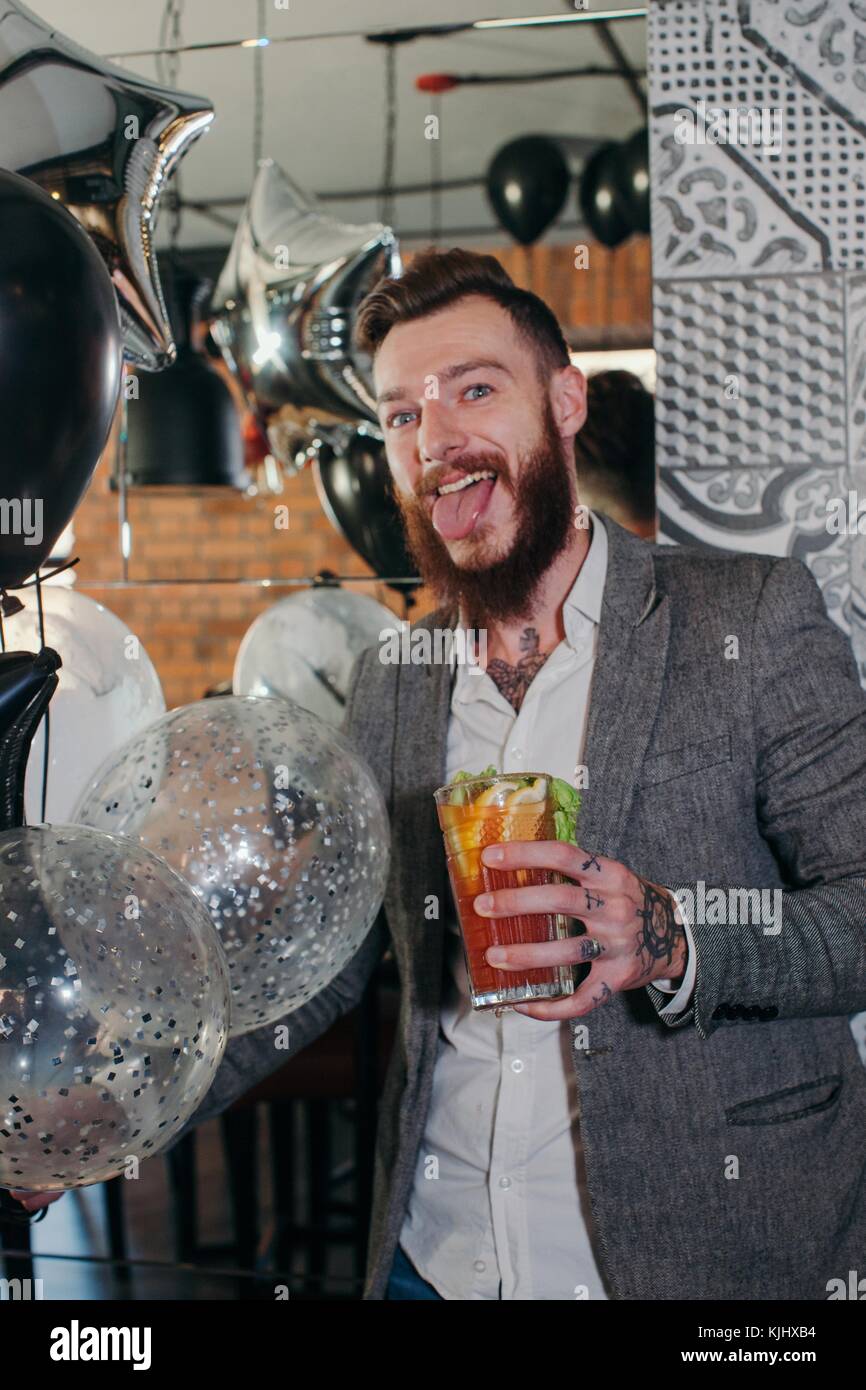 Man standing in a bar with a cocktail sticking out his tongue Stock Photo