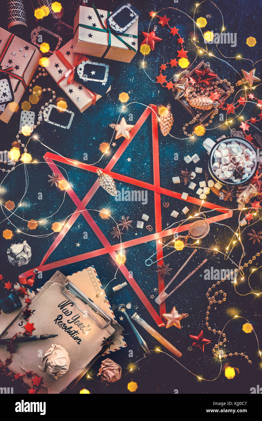 Star of Christmas essentials. Decorations, gift boxes, fairy lights, new year resolution notebook and hot chocolate connected with a red ribbon into a Stock Photo