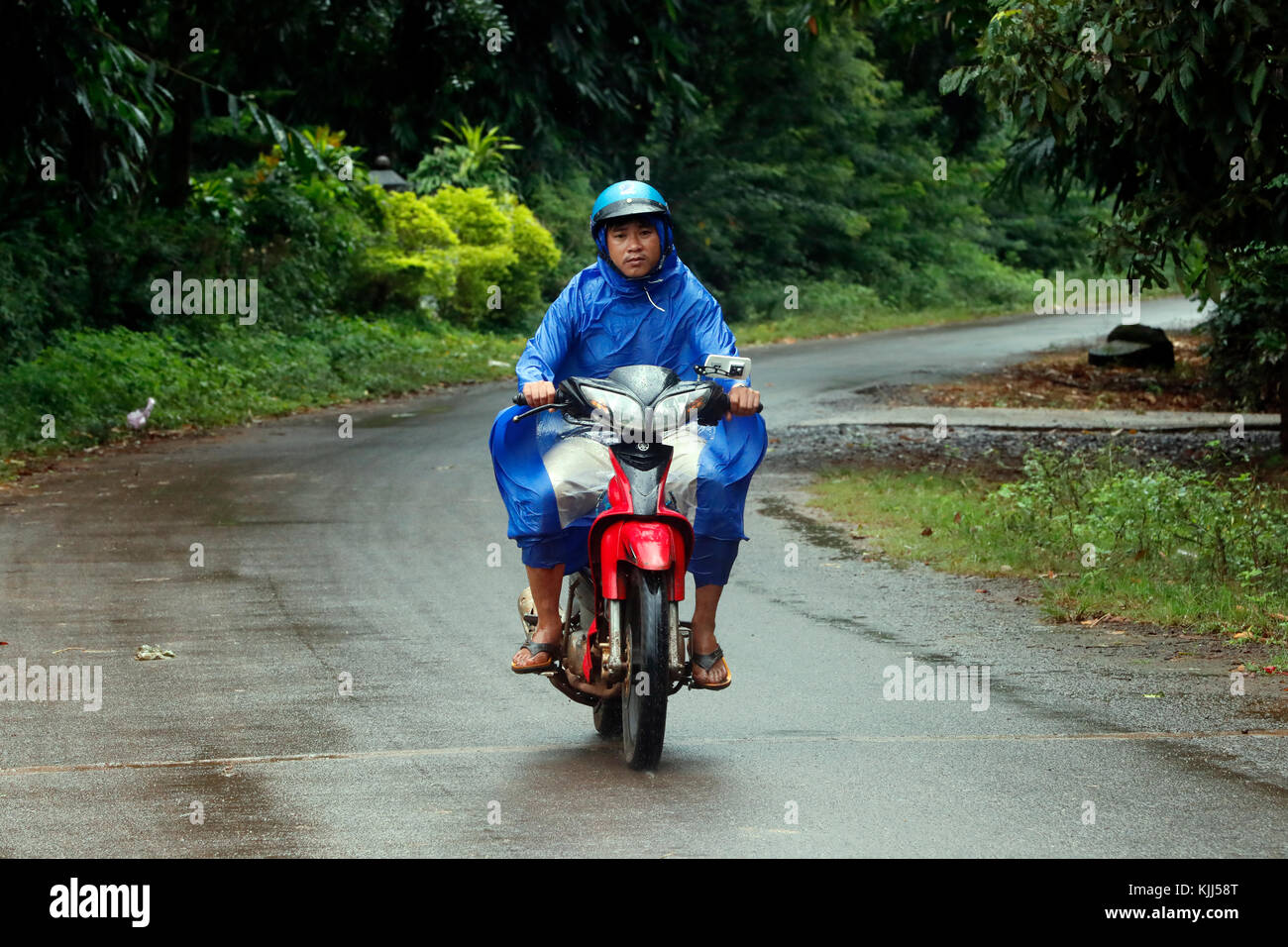 Man driving scooter on a road after rain.  Kon Tum. Vietnam. Stock Photo