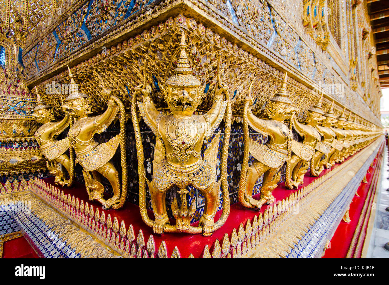 Along the inner walls of the Bangkok Palace complex Wat Phra Kaew temple, a frieze of gilded Garudas hold the Naga snakes to protect the temple. Stock Photo