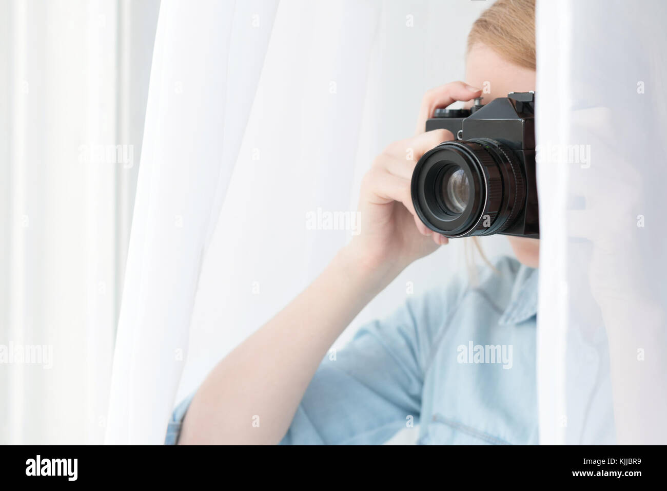 Woman taking pictures through the curtain at window Stock Photo