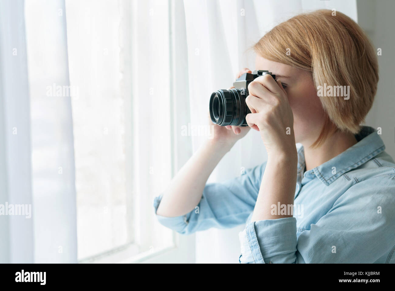 Woman taking photos through the window curtains Stock Photo