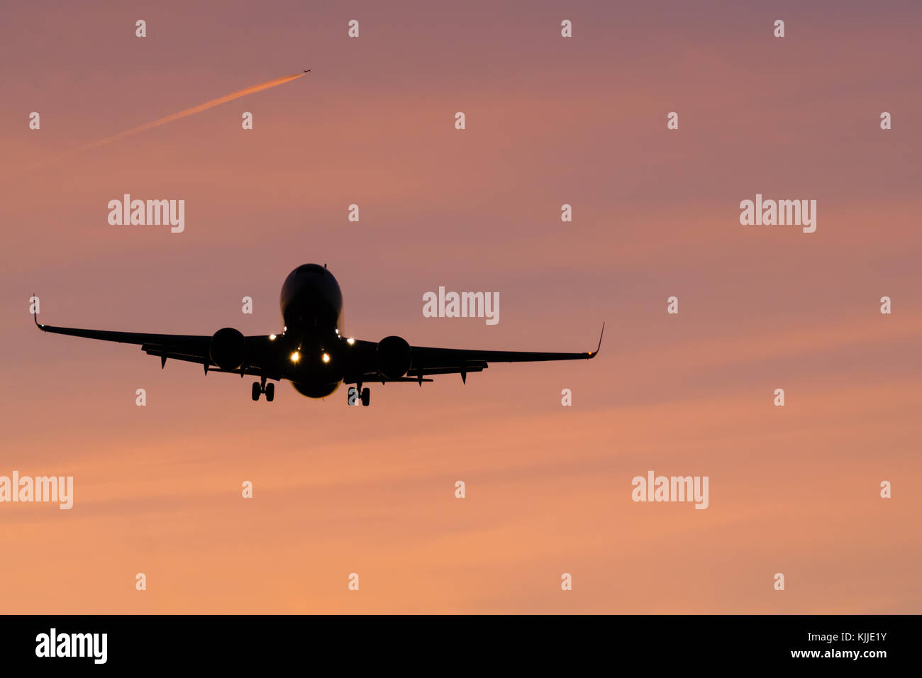 plane will land in orange air and a other plane with fuel outgassing in the background Stock Photo