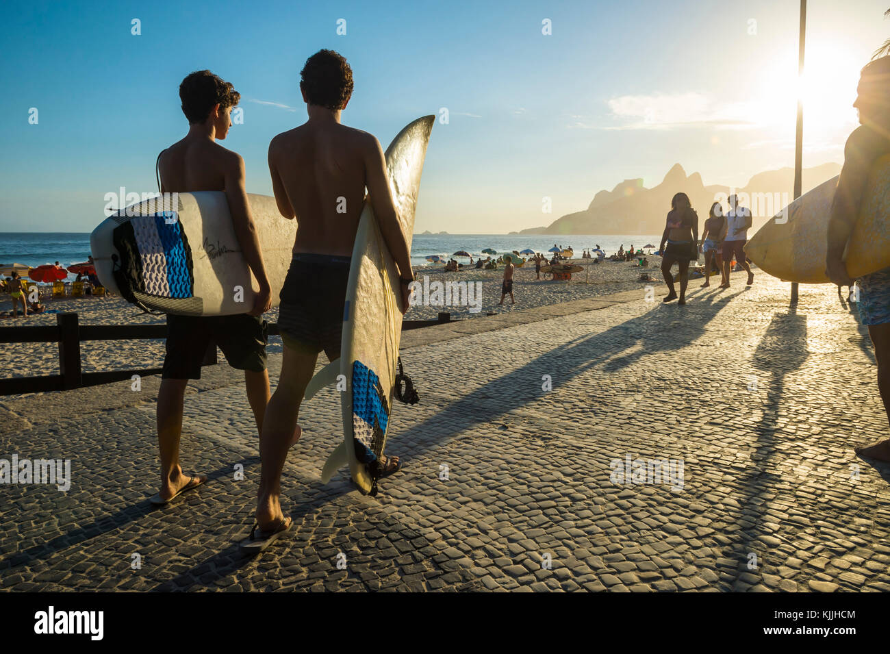 RIO DE JANEIRO - MARCH 24, 2017: Sunset silhouettes of two young surfers walking with surfboards at Arpoador with two brothers mountains in the backgr Stock Photo