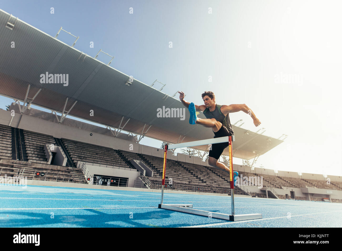 Runner jumping over an hurdle during track and field event. Athlete running a hurdle race in a stadium. Stock Photo
