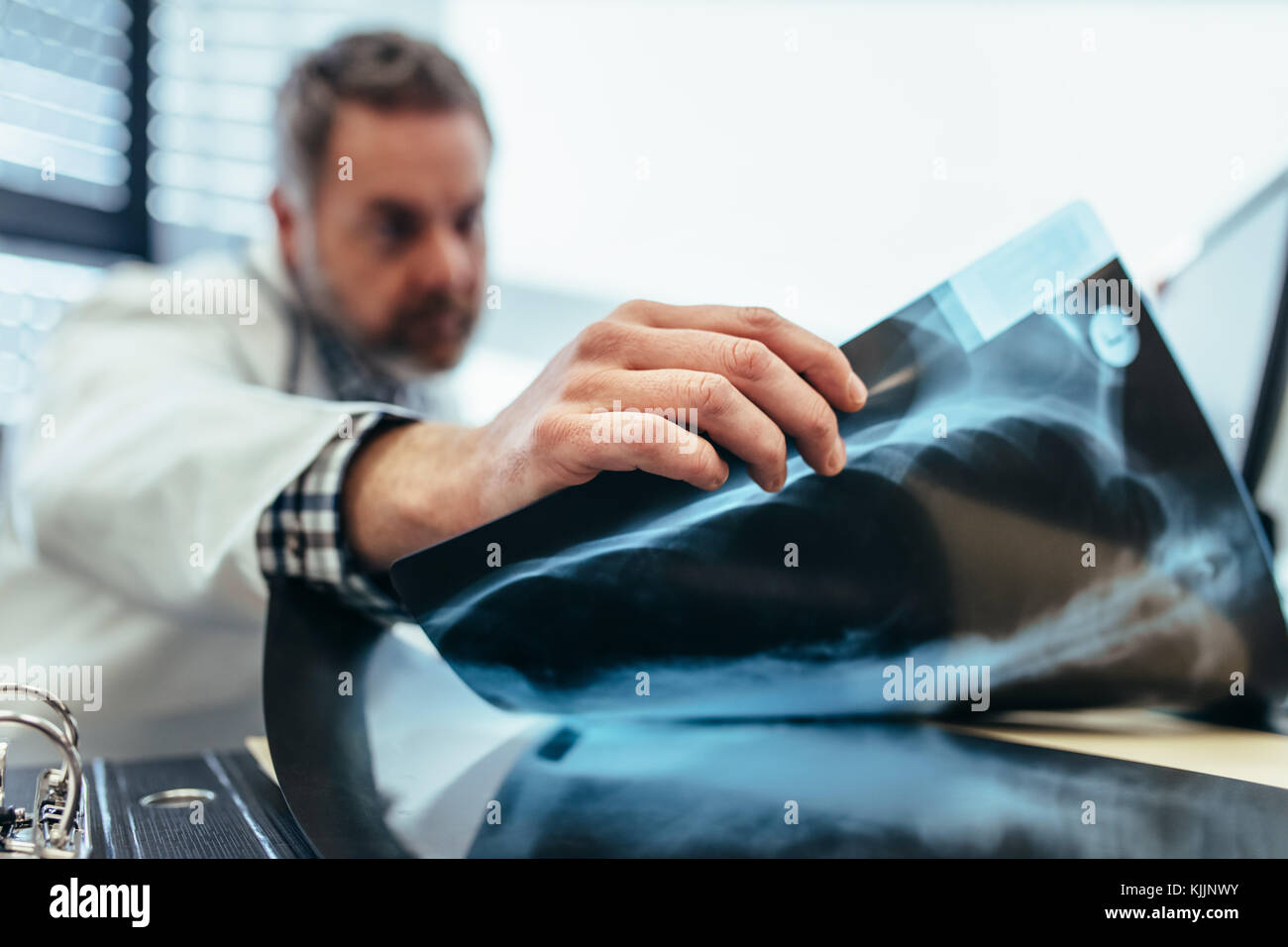 Close up of doctor's hand picking a x-ray from his desk. Male physician sitting in his office and examining medical scan. Stock Photo