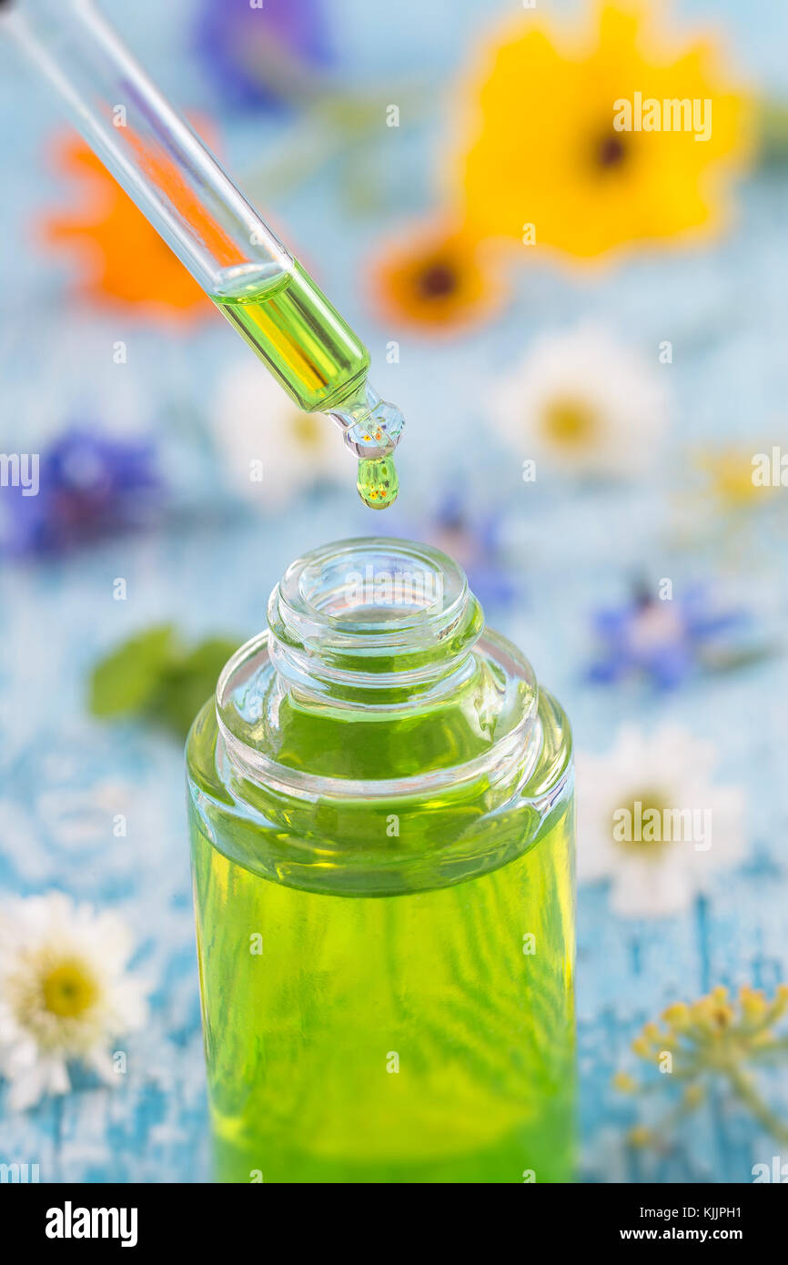 tranparent glass bottles with drops Essential liquid in dropper on wooden background with medicinal flowers Stock Photo