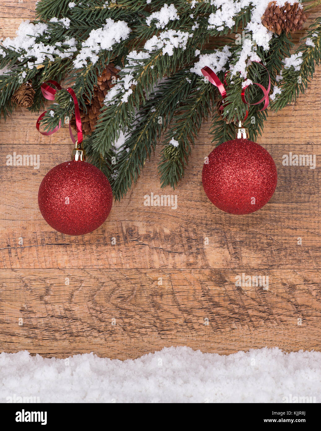 Red Christmas ornaments hanging from a tree branch on a wood background ...
