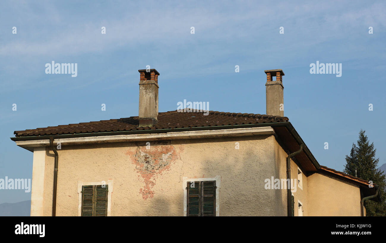 Old and decadent abandoned property roof and chimney detail against blue skies and thin white clouds Stock Photo