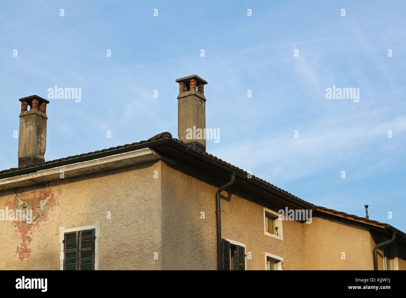 Old and decadent abandoned property roof and chimney detail against blue skies and thin white clouds Stock Photo