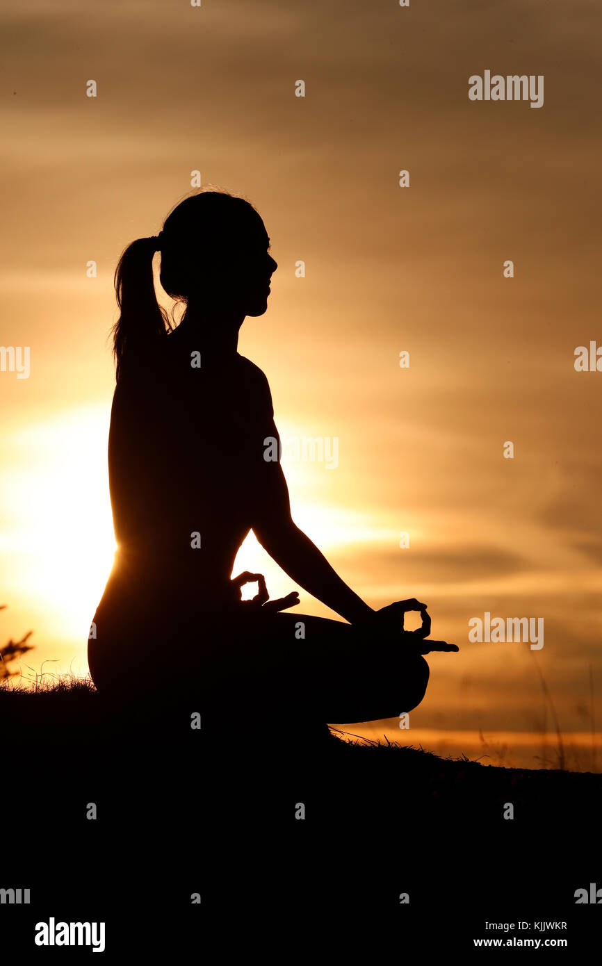 Silhouette of a woman practicing yoga against the light of the evening sun.  Lotus position.  French Alps. France. Stock Photo