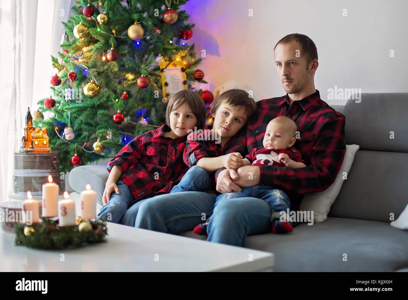 Happy family portrait on Christmas, mother, father and three children sitting on couch at home, chritmas decoration around them Stock Photo