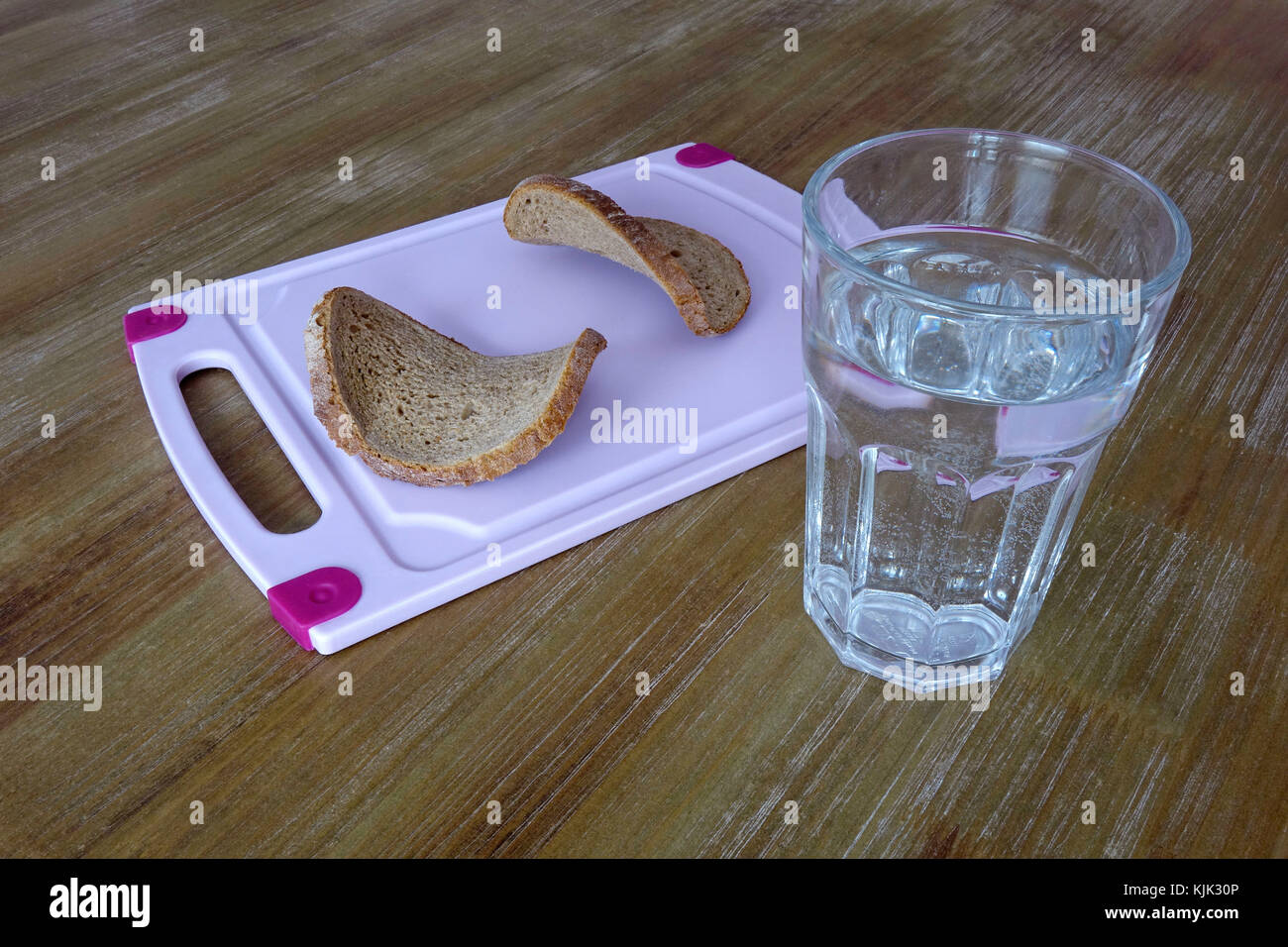 ILLUSTRATION - A glass of water next to a board on which there are two pieces of dry bread, 02.03.2017. In the past 'bread and water' was a punishment prison diet. - KEINE BILDFUNKVERWENDUNG - Foto: Sascha Steinach/dpa-Zentralbild/dpa | usage worldwide Stock Photo
