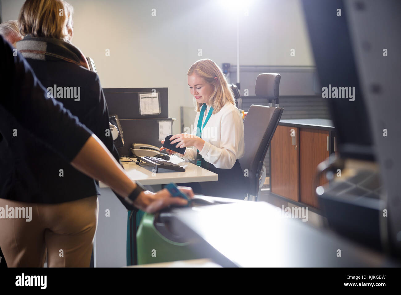 Young female staff examining boarding pass of passenger at airport check-in Stock Photo