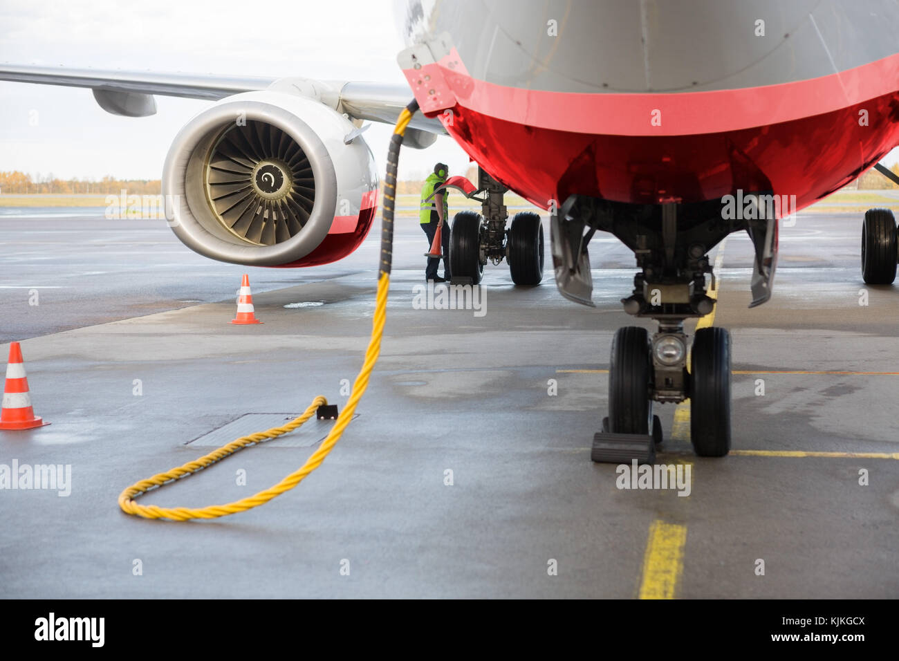 Commercial airplane being charged while worker working on wet runway Stock Photo