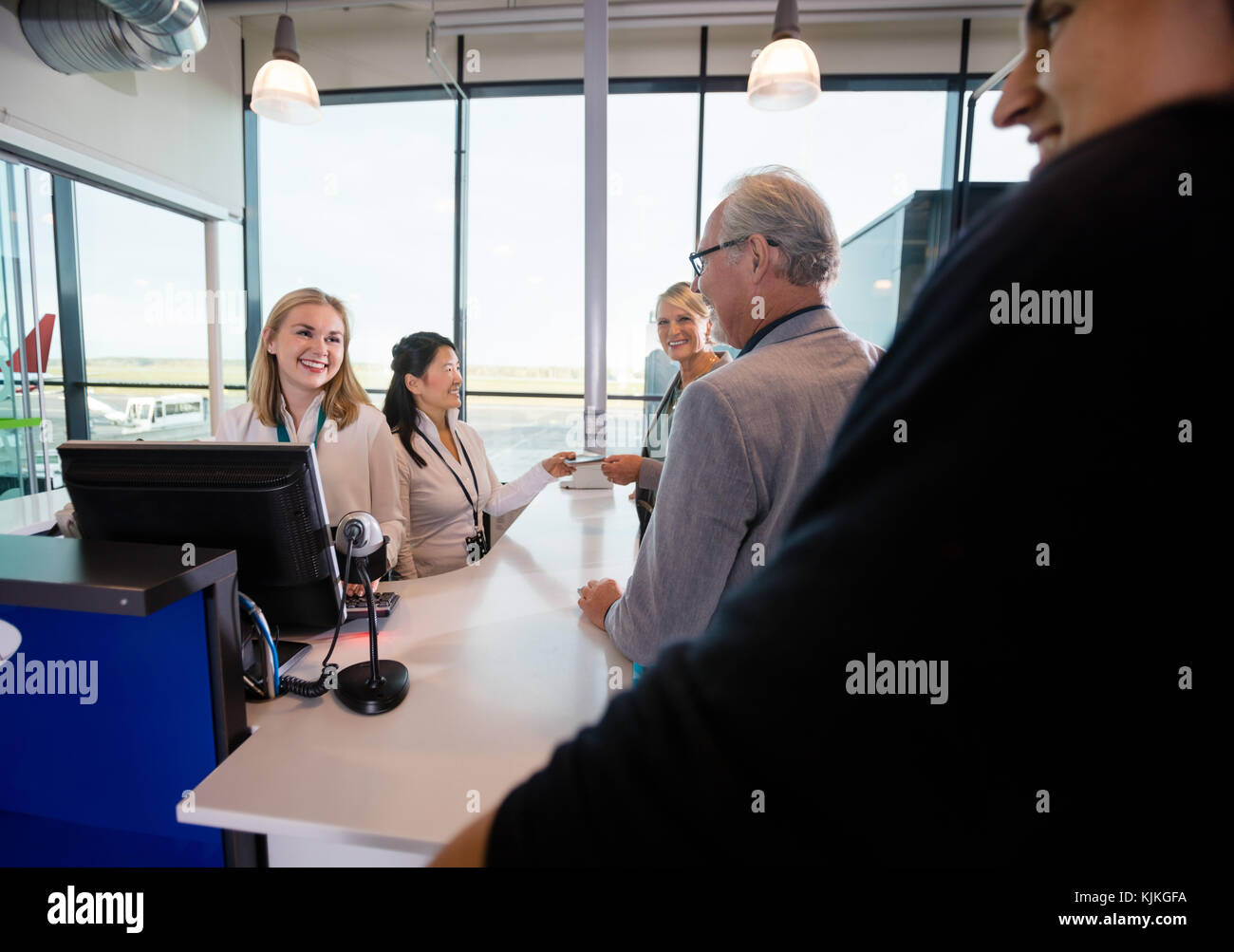 Smiling female staff members looking at passengers at counter in airport Stock Photo