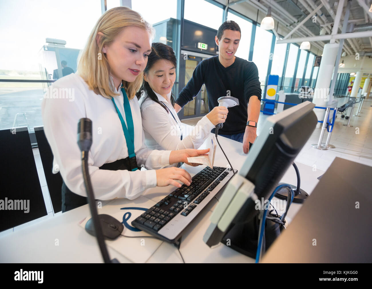Young receptionist entering details of passport in computer while colleague scanning passengers smartwatch in airport Stock Photo