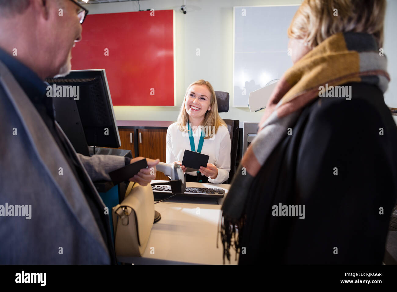 Smiling female staff holding passport while looking at senior business couple in airport Stock Photo